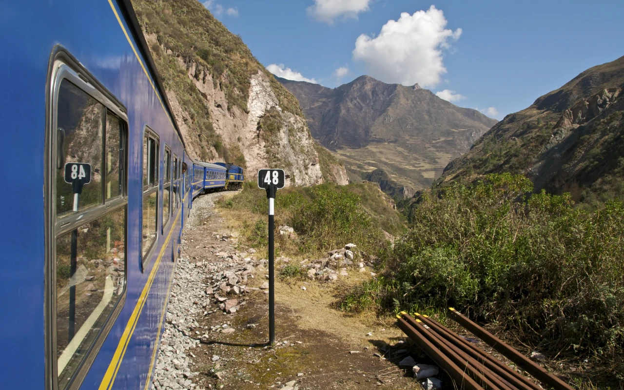 Young backpacker embarks on train journey to Machu Picchu, admiring the stunning Andean landscapes en route.