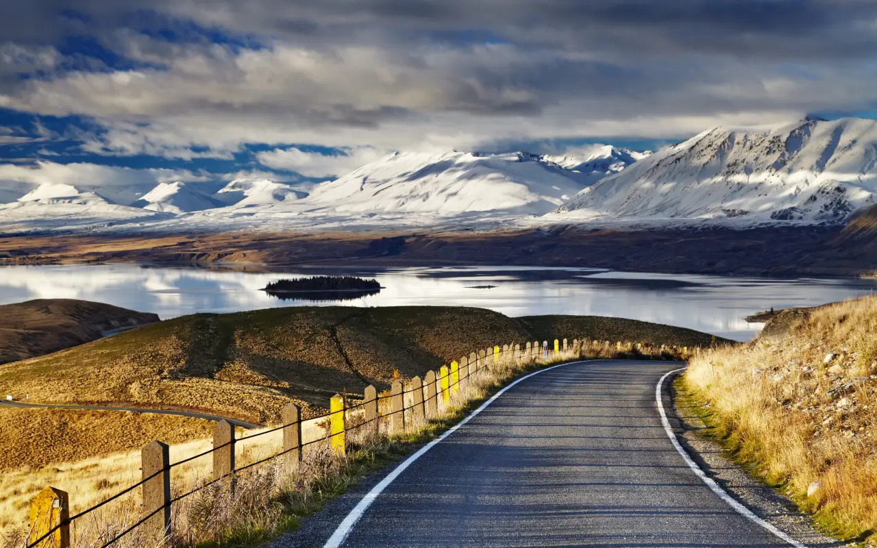 Winding road alongside a lake with snow-capped mountains in the background