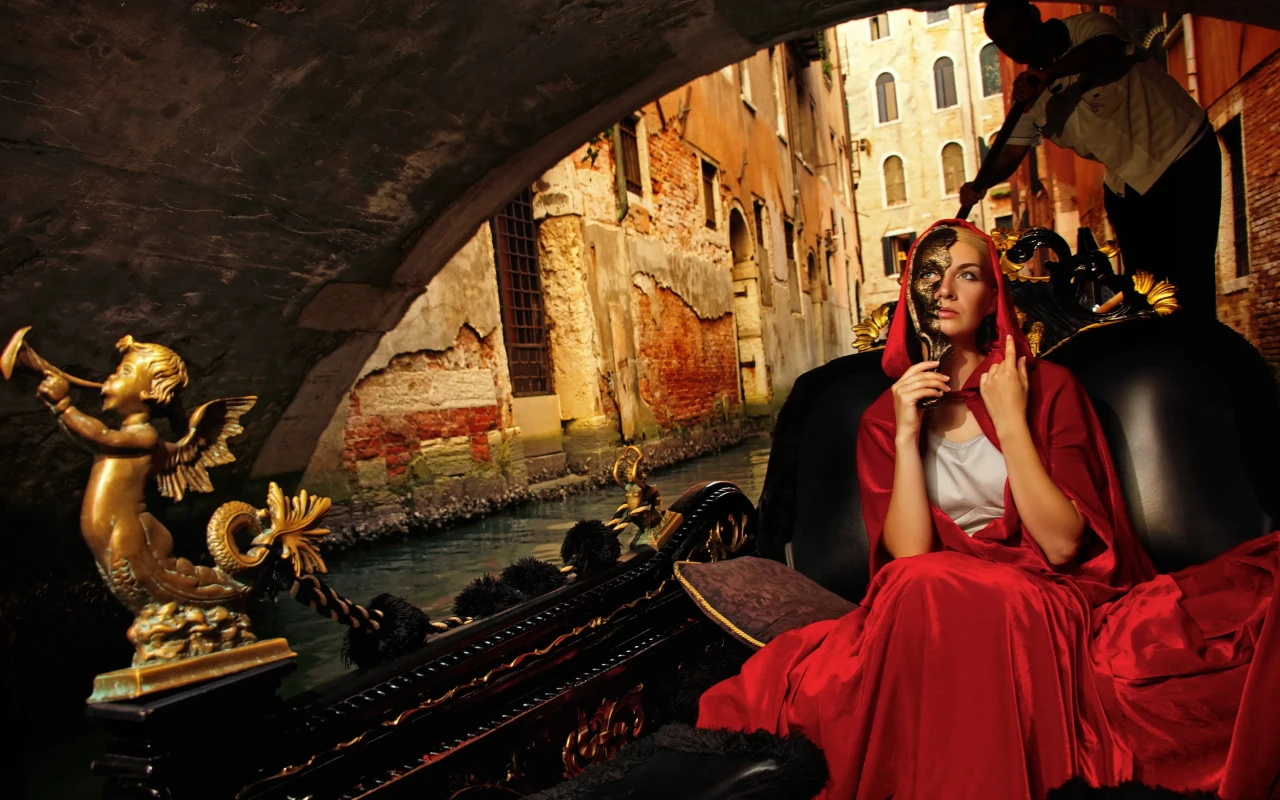 A woman in traditional Venetian carnival costume riding a gondola during the Venice Carnival