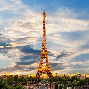 Majestic Eiffel Tower in Paris, France lit up at dusk with a cloudy blue sky backdrop.