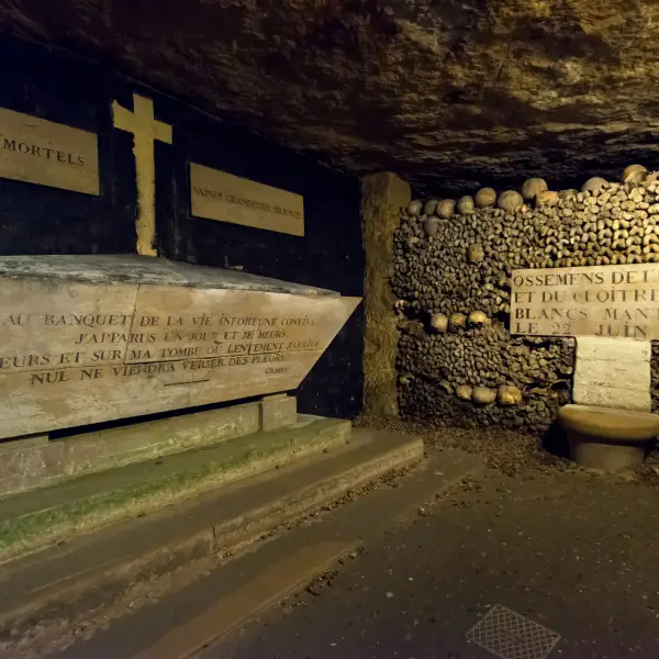 Underground view of the eerie Catacombs of Paris, with walls lined with skulls and bones.