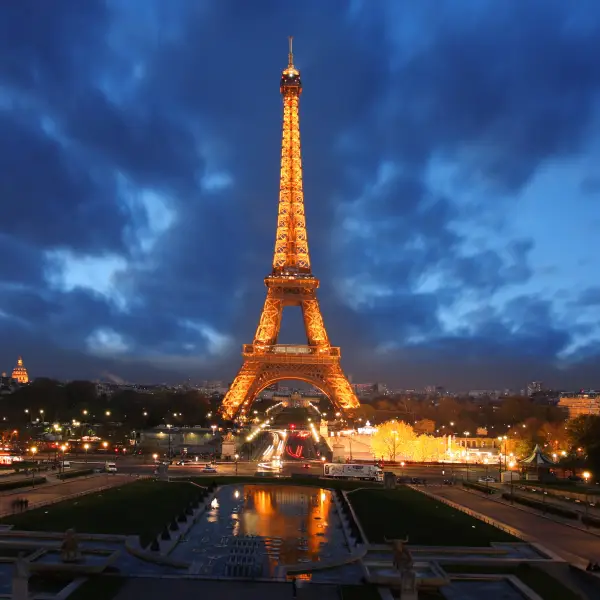 Majestic Eiffel Tower in Paris, France lit up at dusk with a cloudy blue sky backdrop.